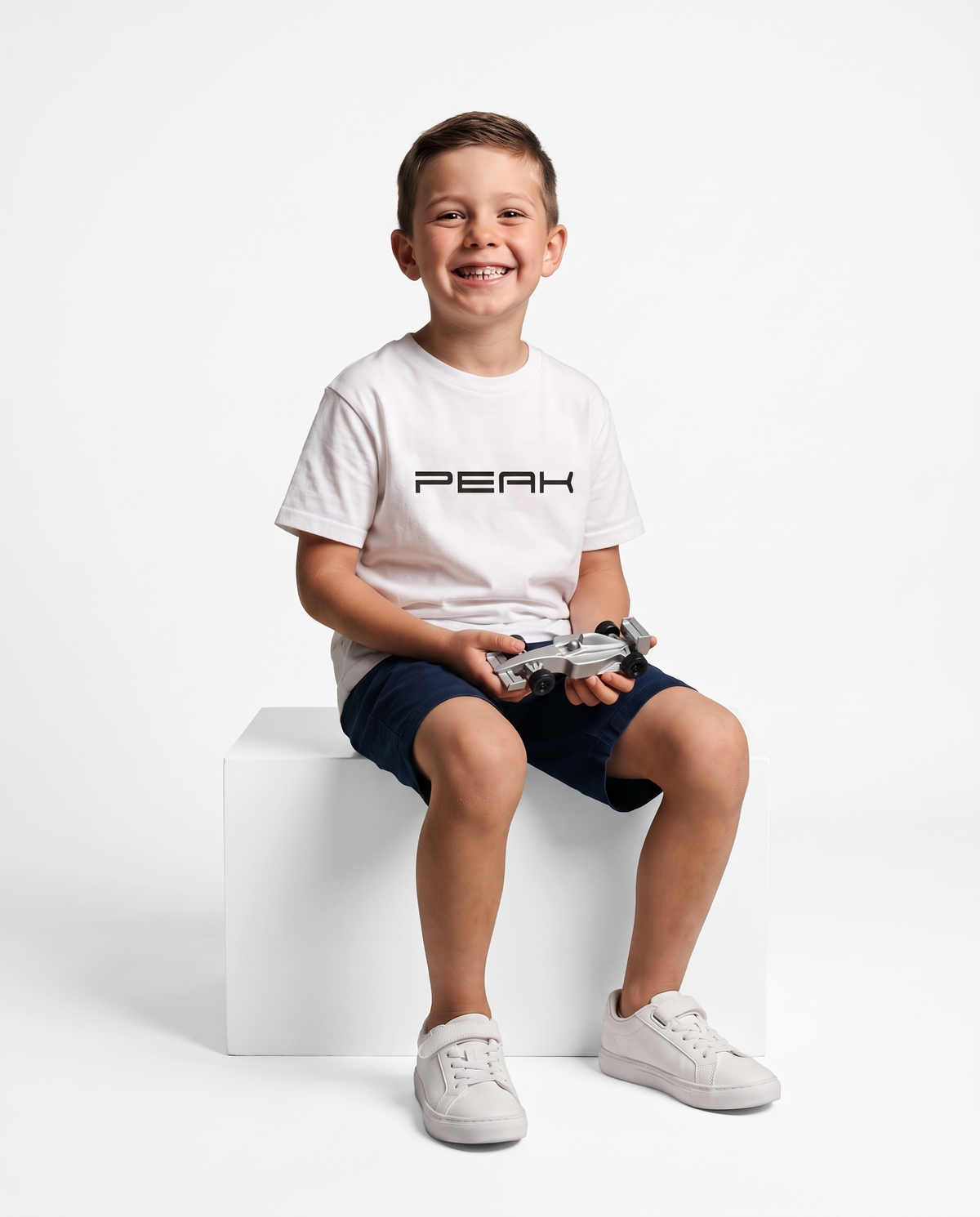 Boy wearing the PEAK Kids Tee in White holding a toy race car