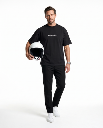 Man wearing the PEAK Heavy Tee in Black, holding a white racing helmet