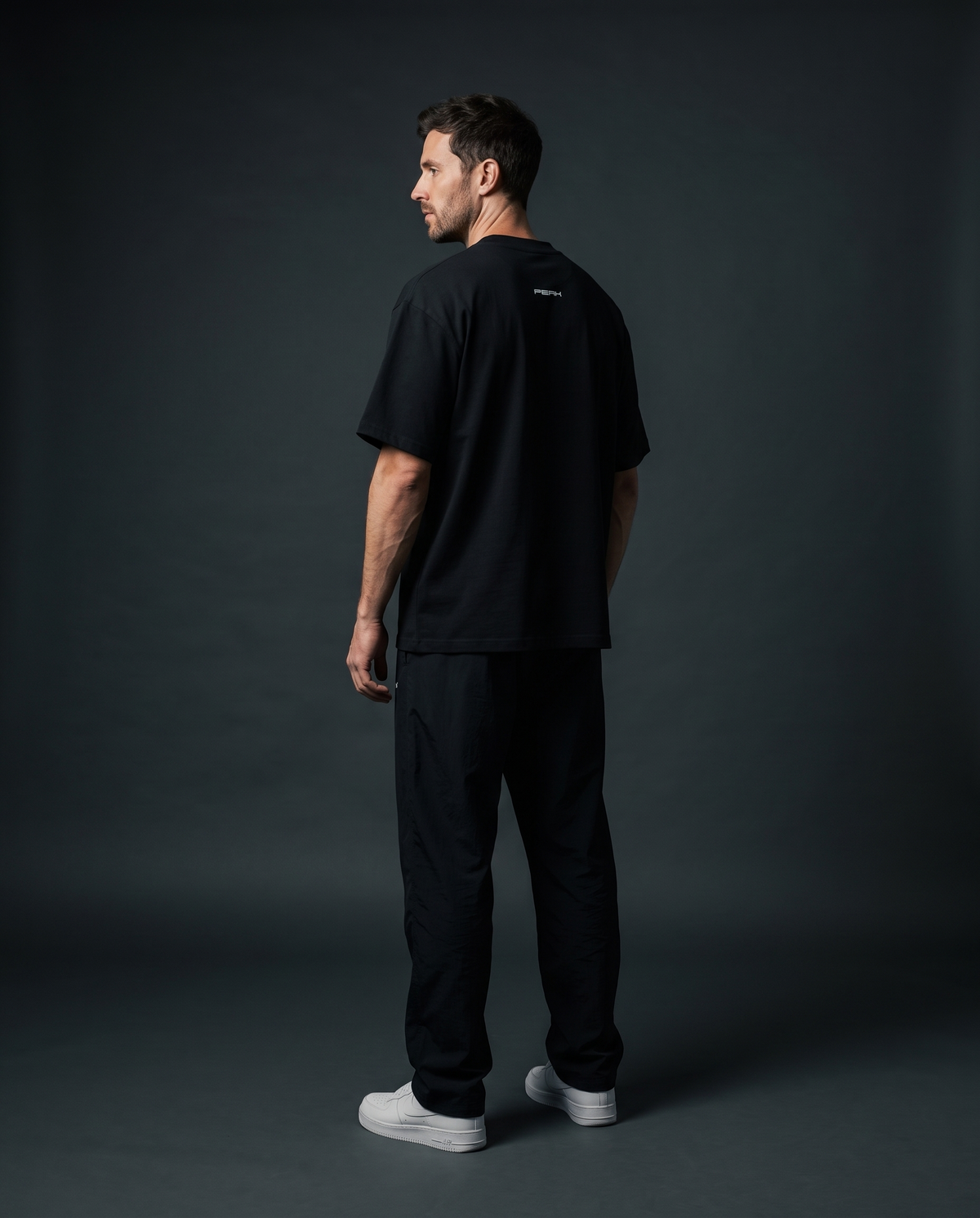 PEAK Back Neck Tee in Black worn in a dark studio