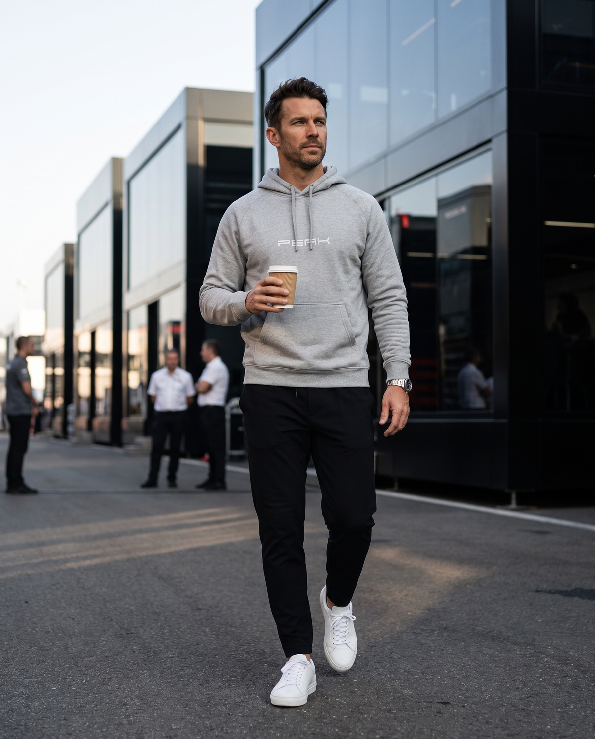 Man wearing the PEAK Supply Hoodie in Grey with a coffee in a race paddock
