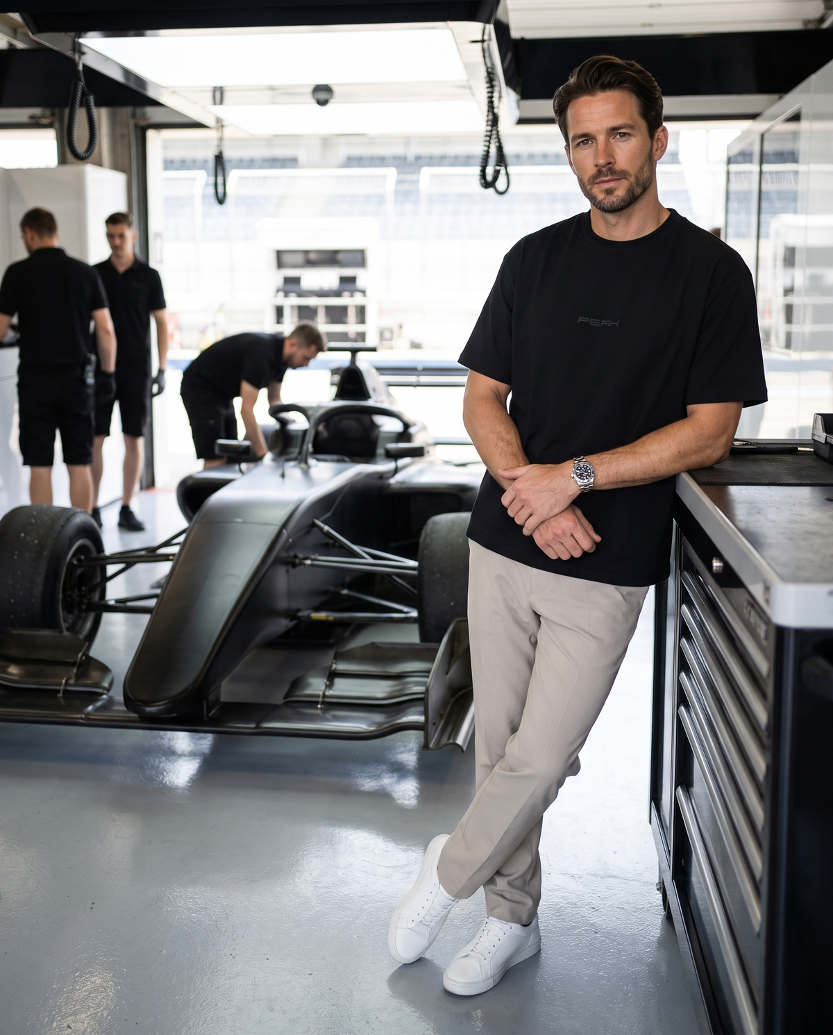 Man wearing the PEAK Tonal Tee in Black in a race team pit garage