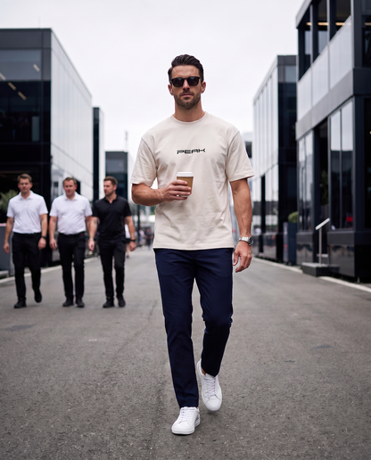 PEAK Heavy Tee in Ecru worn walking through a race paddock with a coffee
