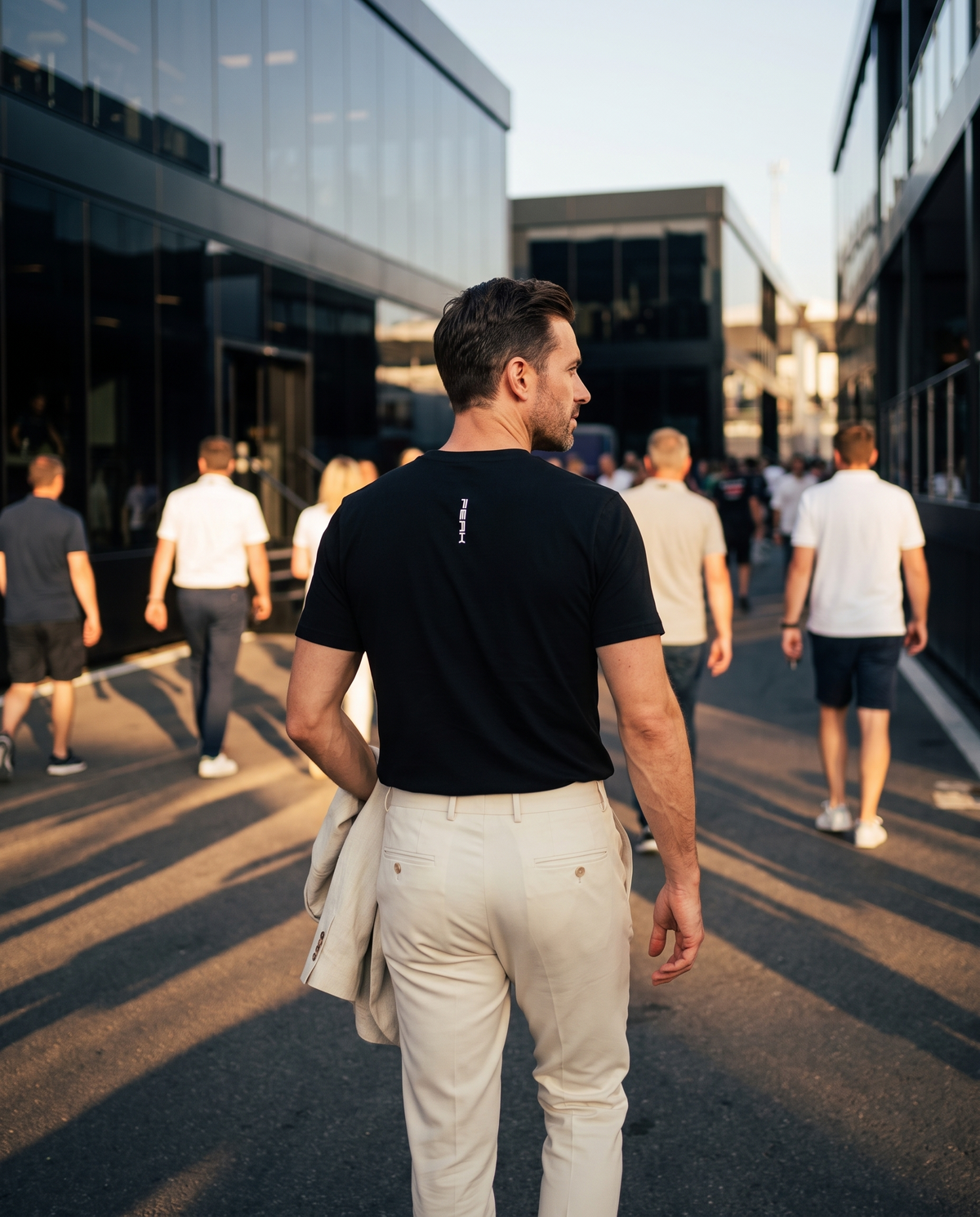 Back view of the PEAK Tee, Chest & Spine Print showing the spine wordmark in a race paddock at golden hour