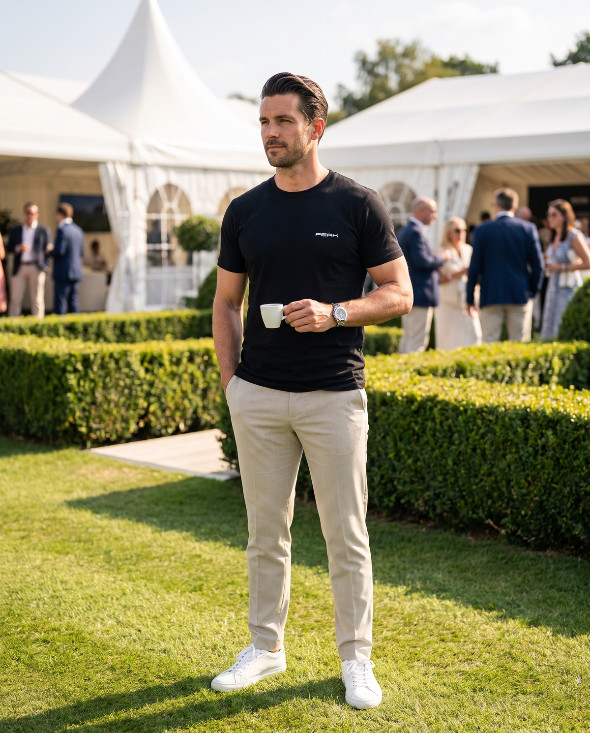 Man wearing the PEAK Tee, Chest & Spine Print in Black on the lawn at a grand prix hospitality garden