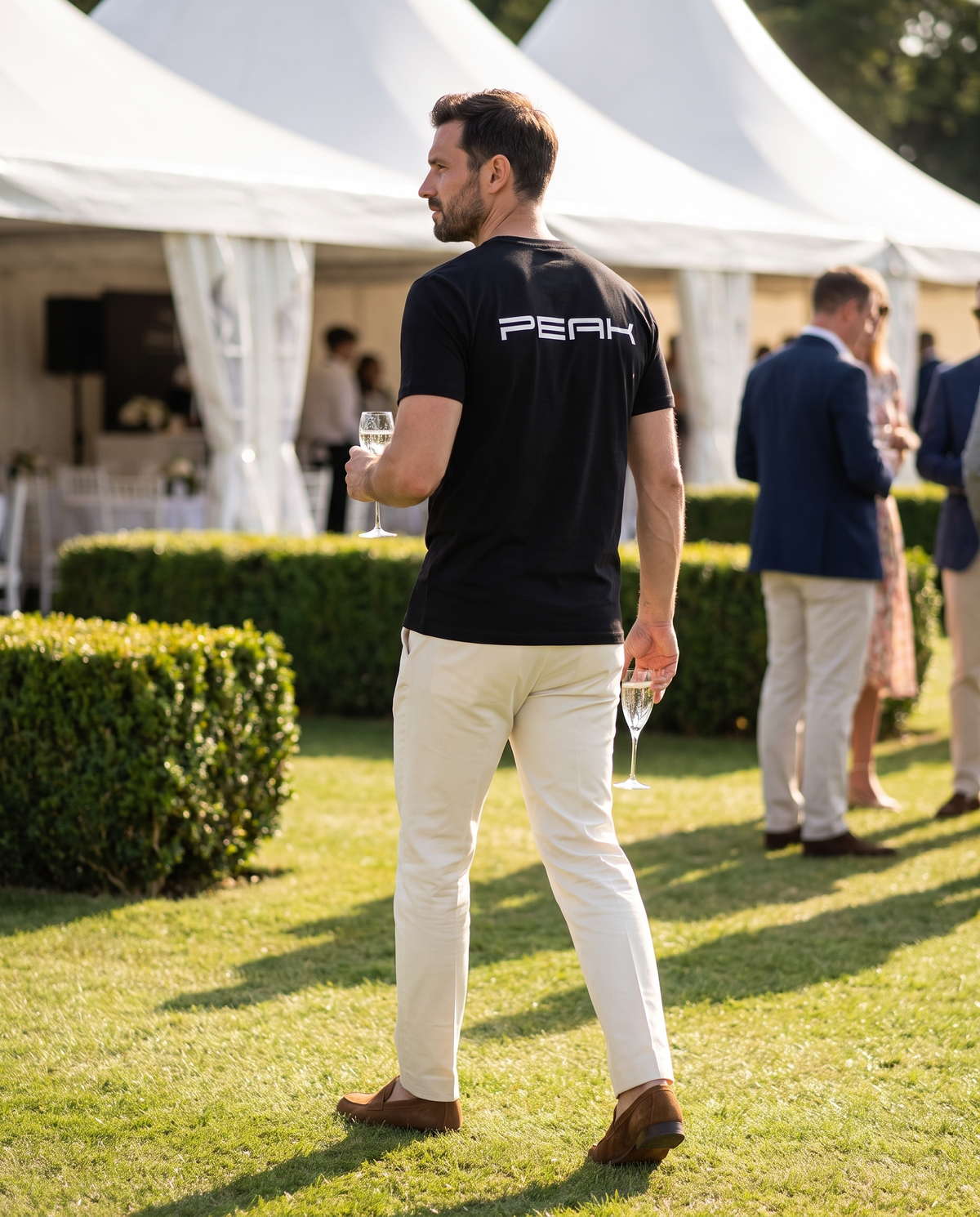 Back view of the PEAK Tee wordmark back print at a grand prix hospitality garden