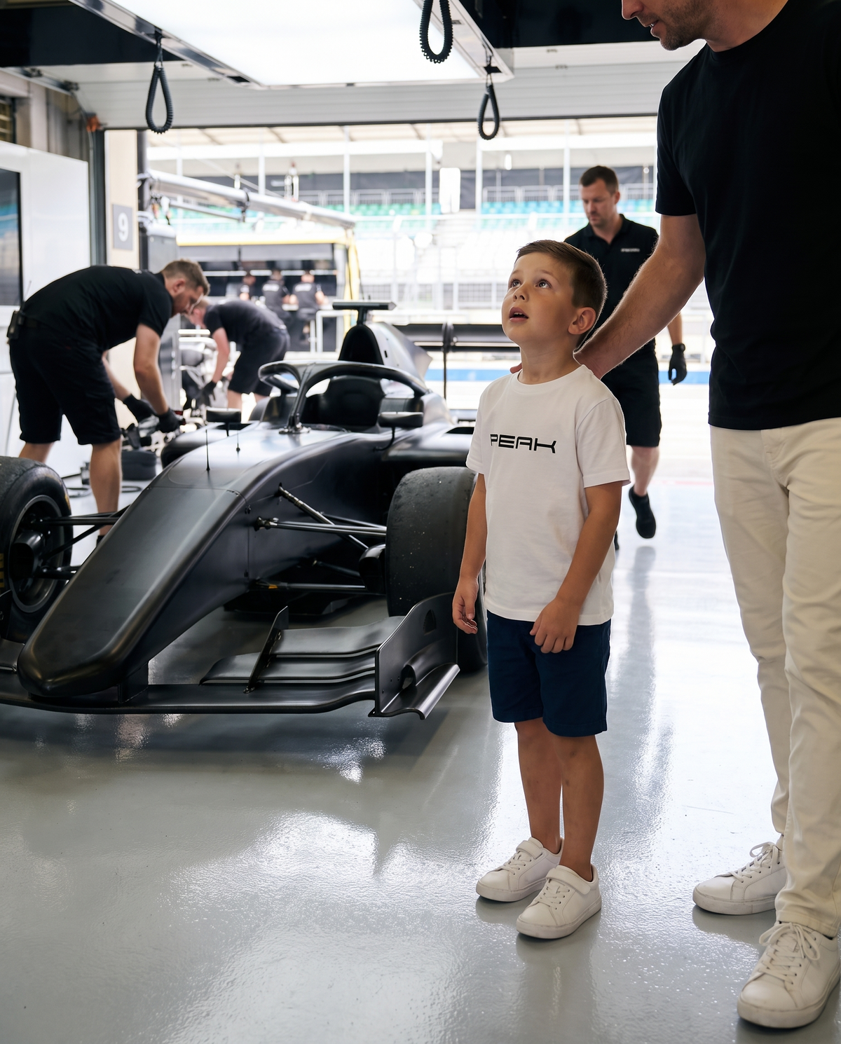 Boy wearing the PEAK Kids Tee in White looking at a race car on a pit garage tour