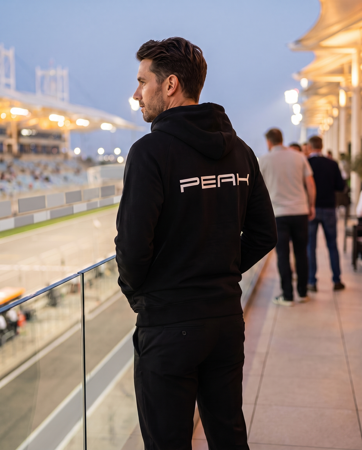 PEAK Supply Hoodie back print worn on a race weekend terrace at dusk