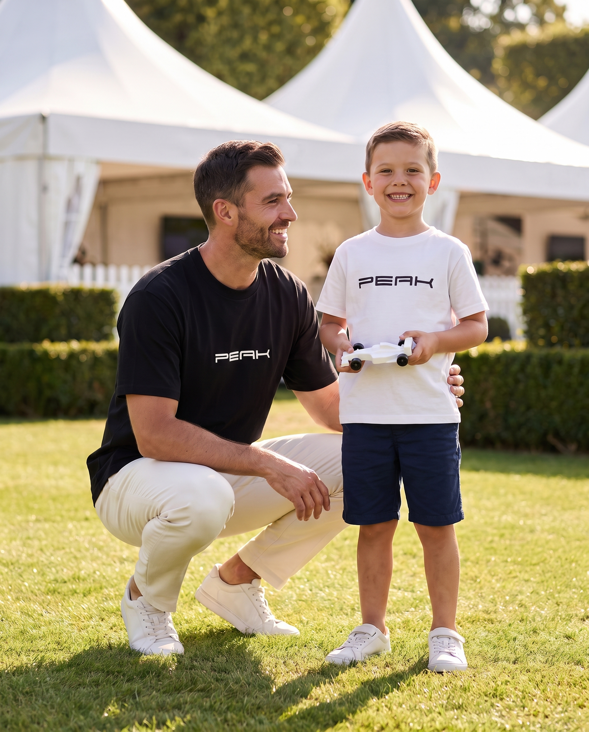Boy in the PEAK Kids Tee in White with his dad in the PEAK Heavy Tee at a grand prix hospitality garden