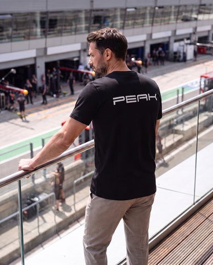 Back view of the PEAK Tee wordmark back print on a terrace overlooking the pit lane