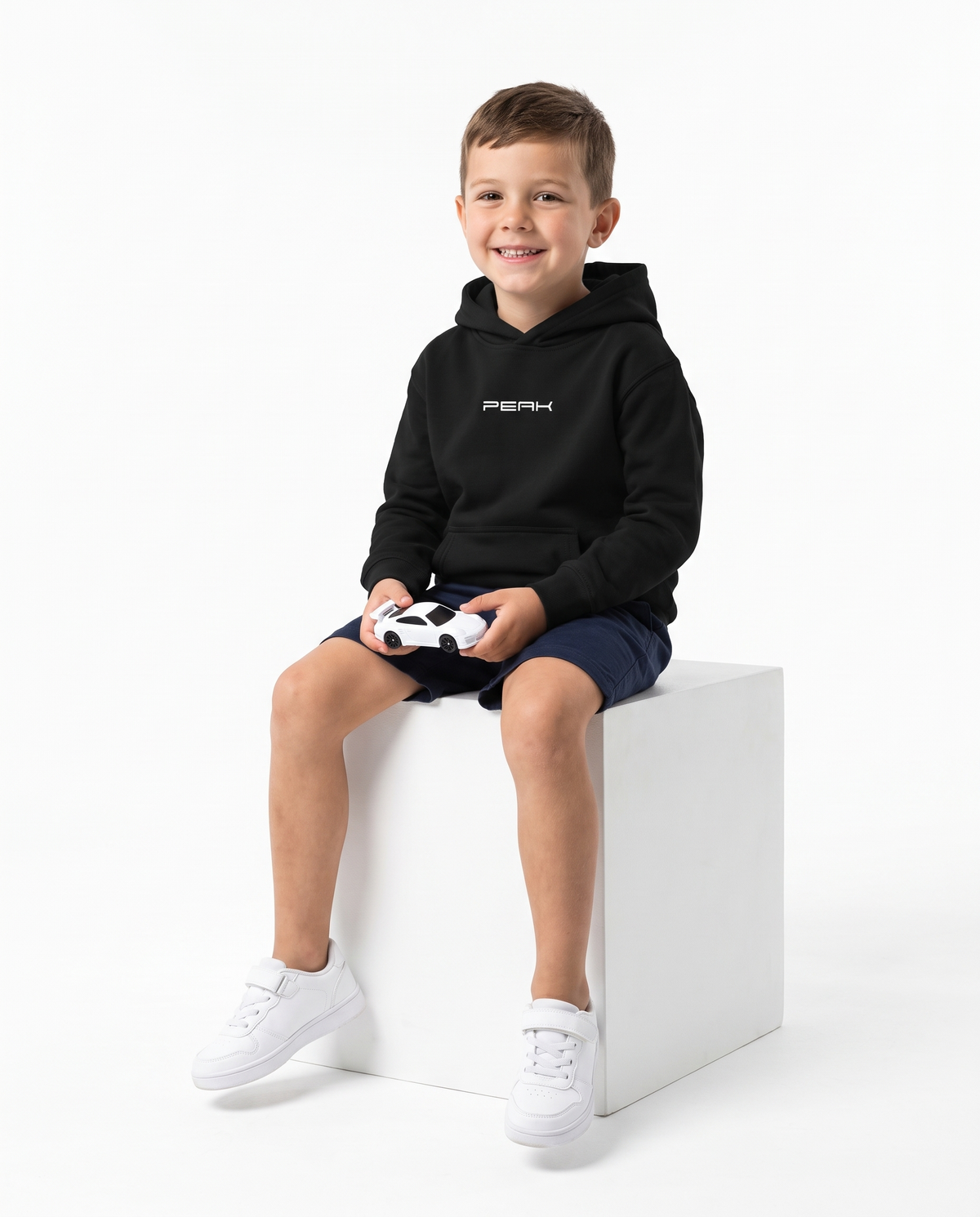 Boy wearing the PEAK Kids Hoodie in Black holding a toy race car